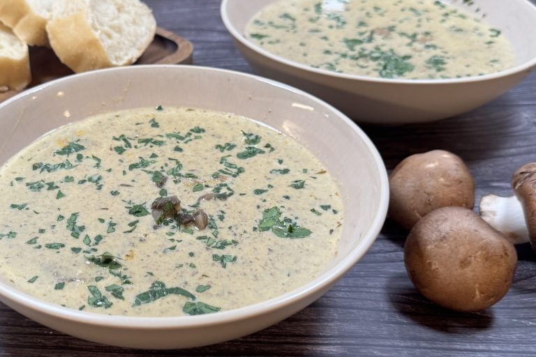 Bowl of creamy mushroom soup garnished with chopped parsley, served with sliced bread and fresh mushrooms on the side.