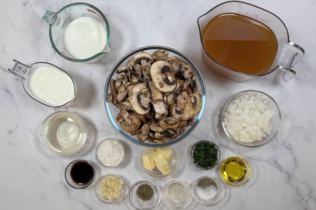 Ingredients for creamy mushroom soup including sliced mushrooms, diced onion, garlic, butter, olive oil, flour, chicken broth, milk, Worcestershire sauce, dried thyme, parsley, salt, and black pepper.