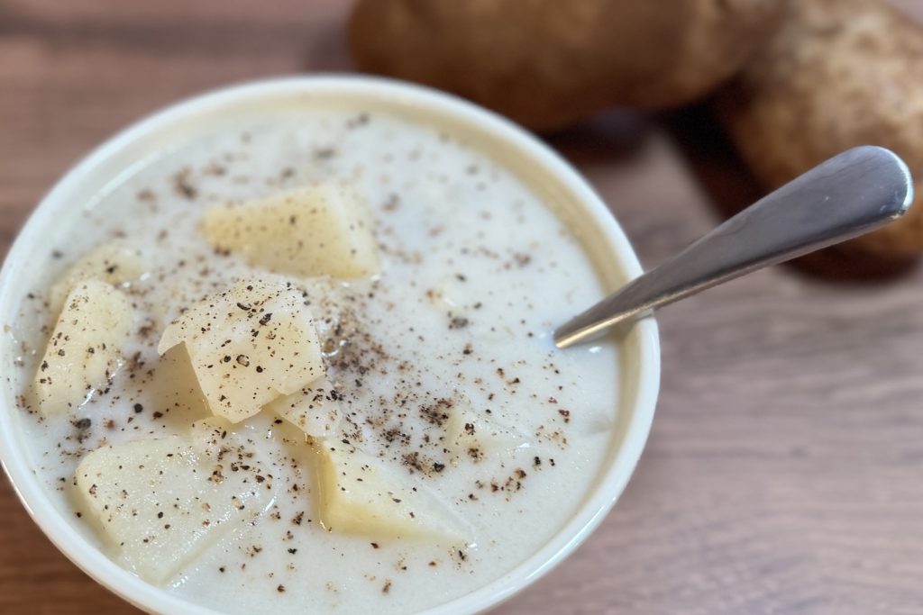 Creamy potato soup topped with cracked black pepper and butter, served in a white bowl with a spoon.