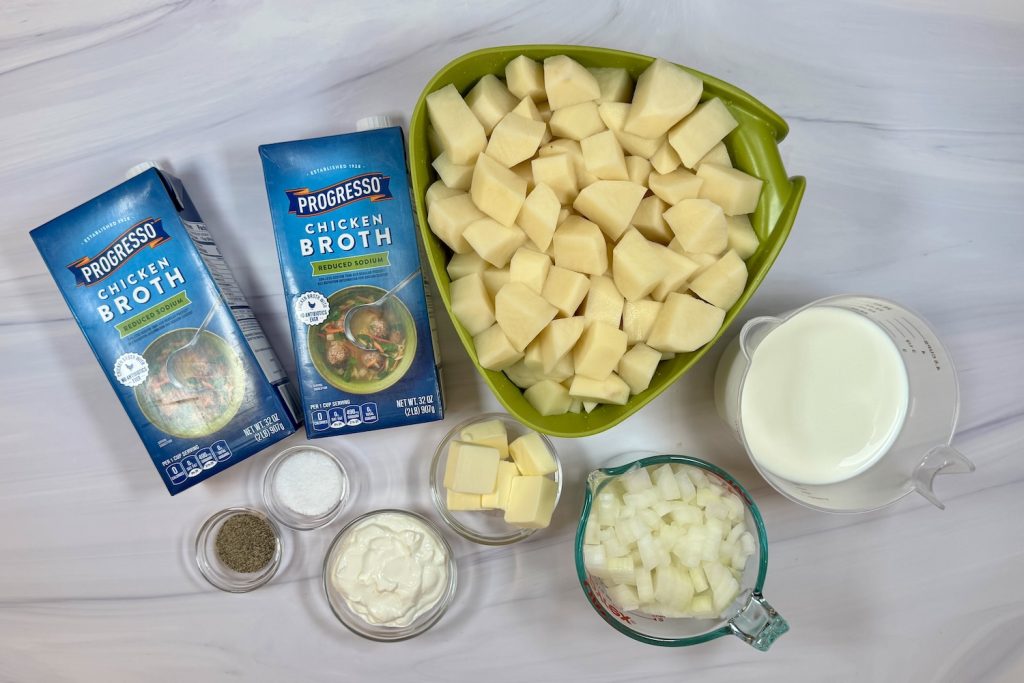 Ingredients for creamy potato soup including chopped potatoes, onion, butter, sour cream, milk, and chicken broth.