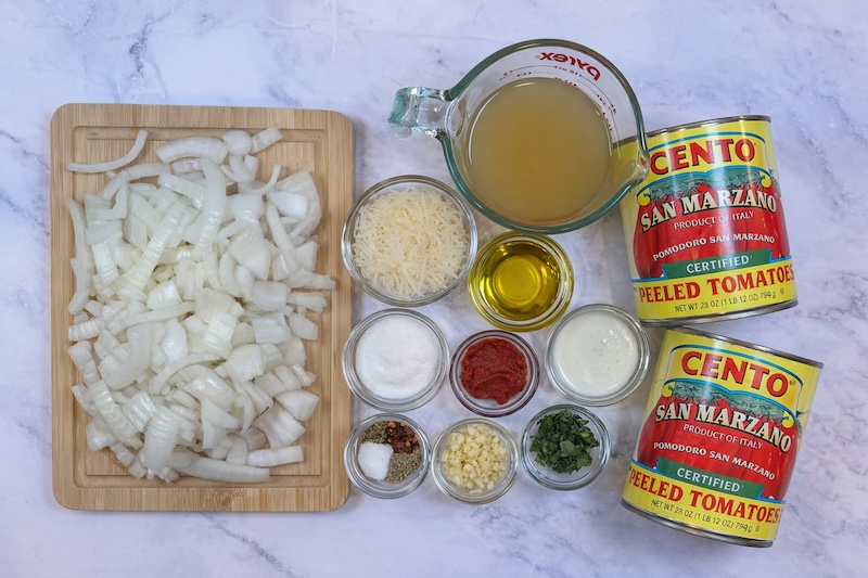 Ingredients for creamy tomato soup including canned tomatoes, onion, garlic, cream, and basil
