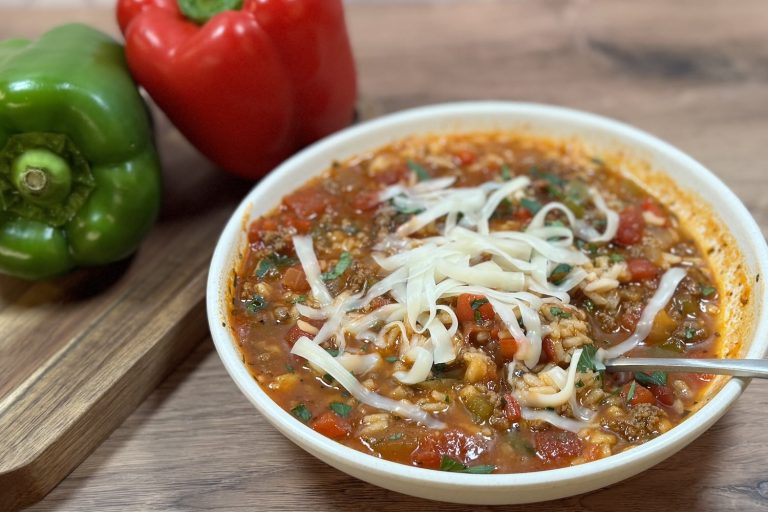 Bowl of stuffed pepper soup topped with shredded mozzarella, made with ground beef, rice, diced tomatoes, and green and red bell peppers in a rich tomato broth.