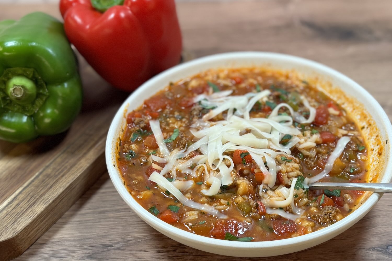 Bowl of stuffed pepper soup topped with shredded mozzarella, made with ground beef, rice, diced tomatoes, and green and red bell peppers in a rich tomato broth.