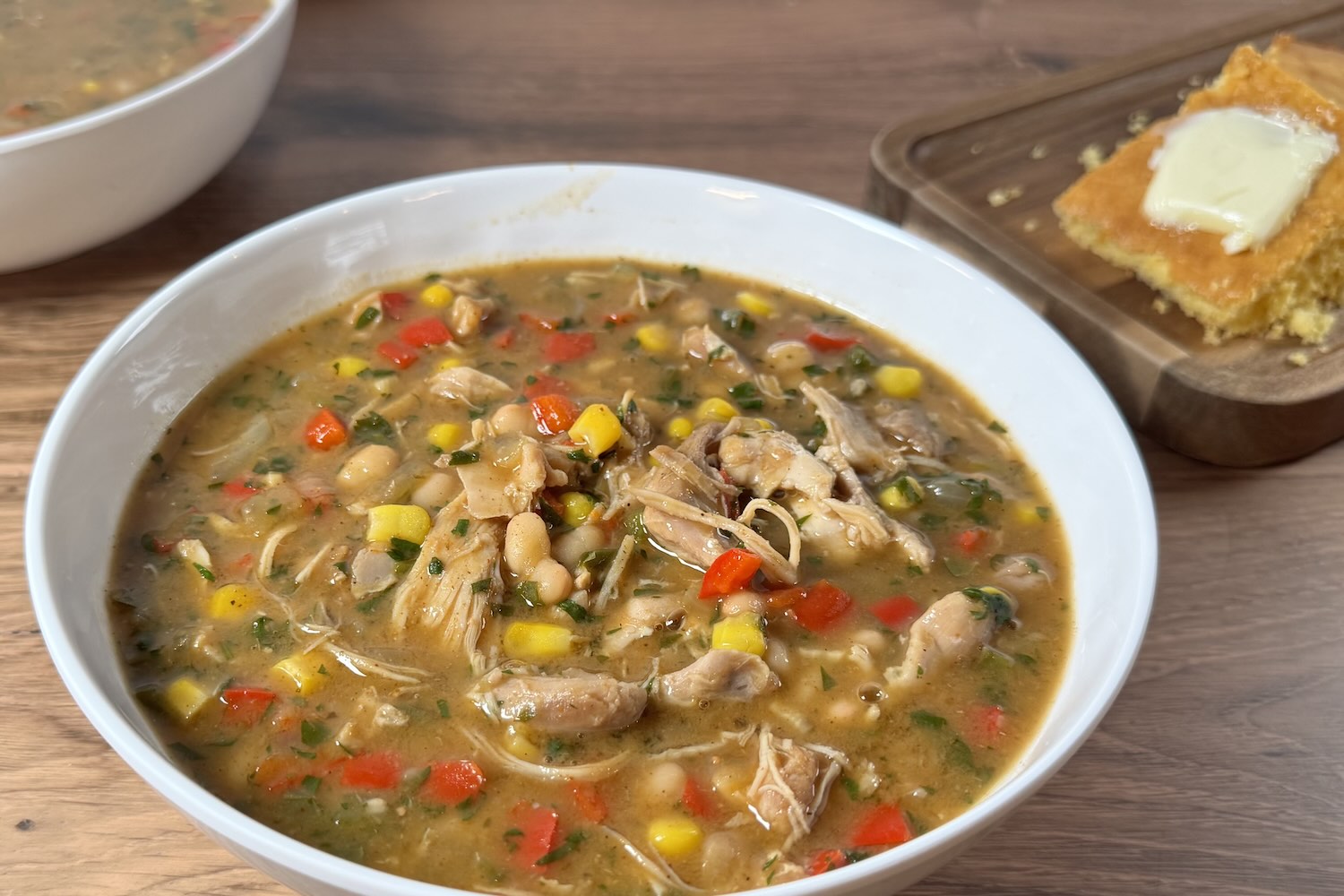 Bowl of white bean chicken chili made with shredded chicken, white beans, corn, diced red and green peppers, and fresh herbs, served with cornbread on the side.
