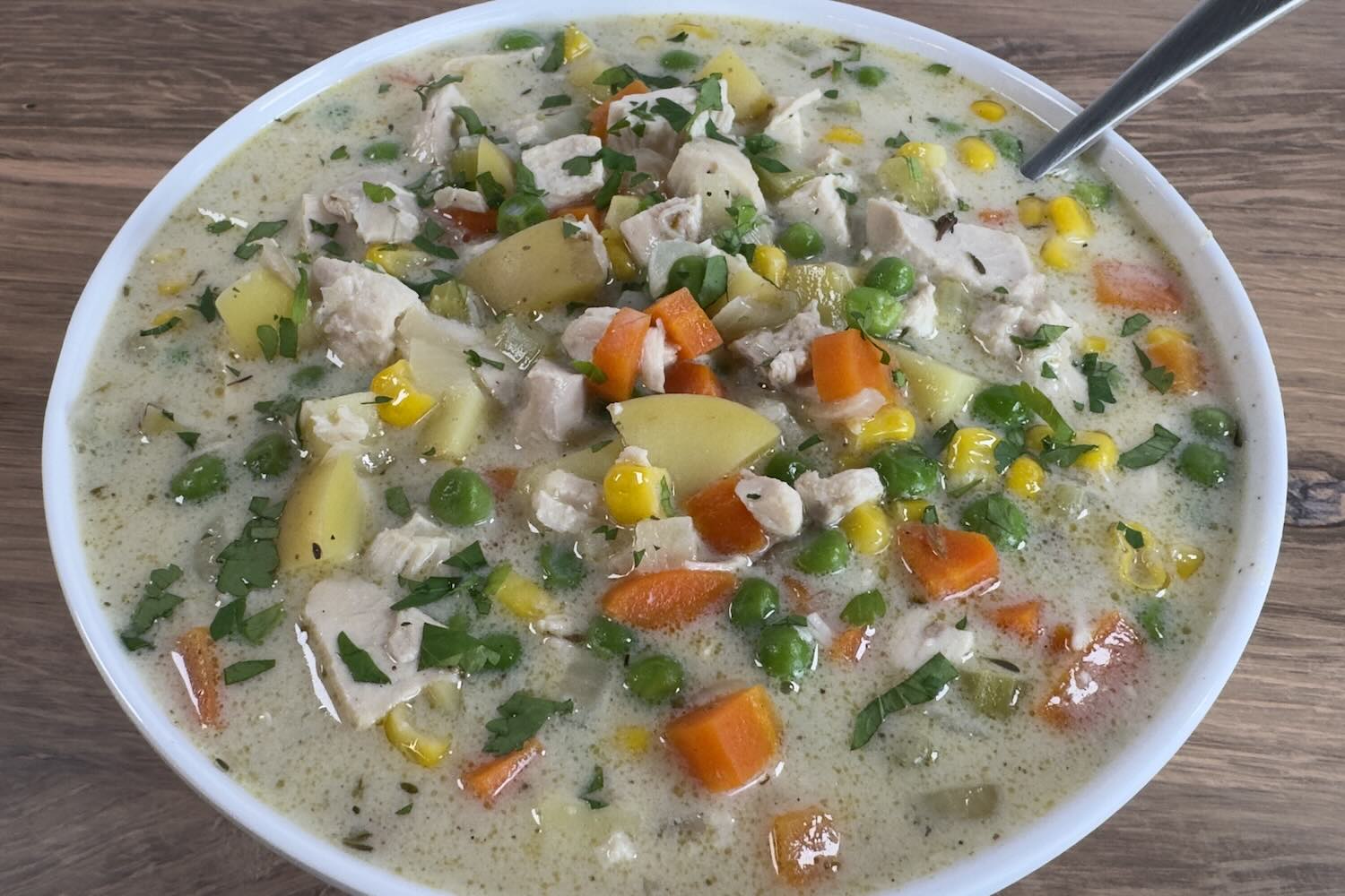 Bowl of chicken pot pie soup with chunks of chicken, potatoes, carrots, peas, and corn in a creamy herb broth.