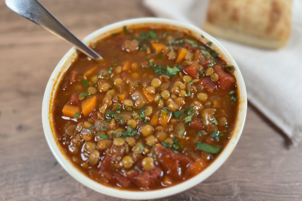 Bowl of easy one-pot lentil soup with carrots, celery, diced tomatoes, and herbs in a rich tomato-based broth, served with bread on the side.