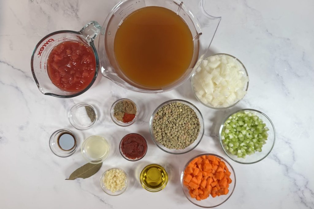 Ingredients for easy one-pot lentil soup including dried lentils, diced tomatoes, vegetable broth, onion, celery, carrots, garlic, olive oil, tomato paste, bay leaf, Worcestershire sauce, lemon juice, and spices.