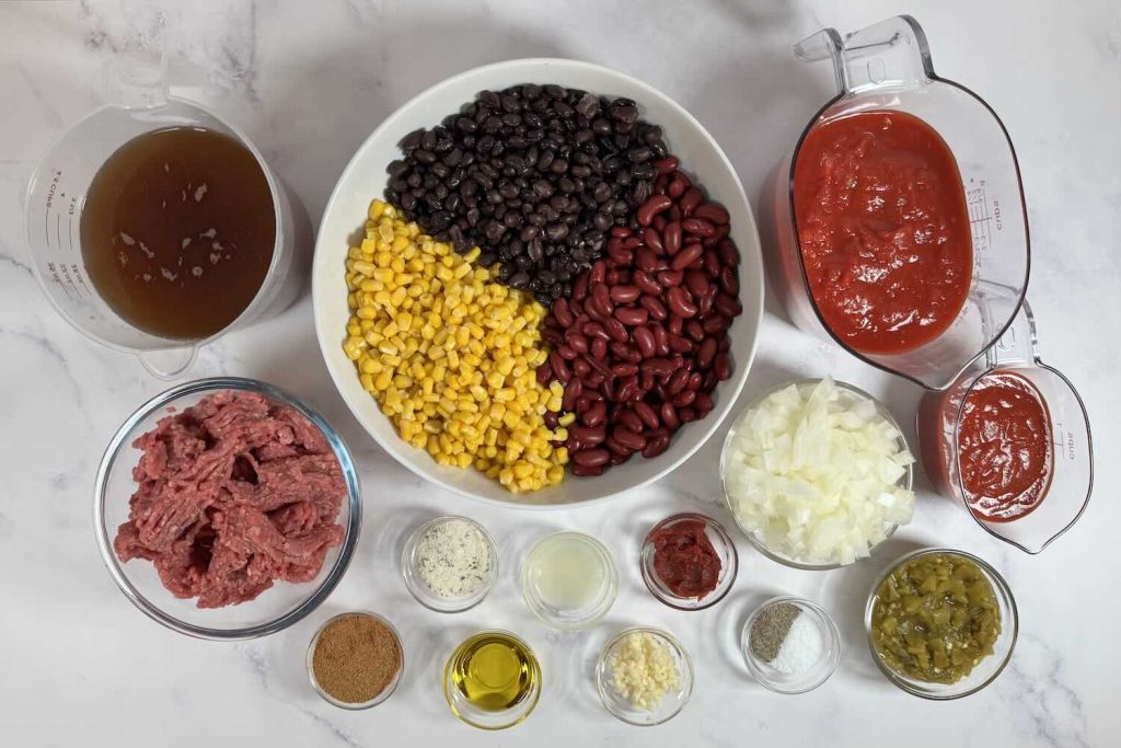 Ingredients for easy taco soup including ground beef, black beans, kidney beans, corn, diced tomatoes, tomato sauce, beef broth, onion, garlic, green chiles, olive oil, taco seasoning, and lime juice.