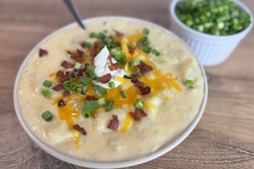Bowl of loaded baked potato soup topped with shredded cheddar cheese, crispy bacon, sour cream, and sliced green onions.
