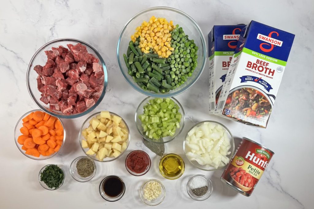 Ingredients for beef vegetable soup including beef stew meat, potatoes, carrots, celery, onion, mixed vegetables, diced tomatoes, and beef broth.