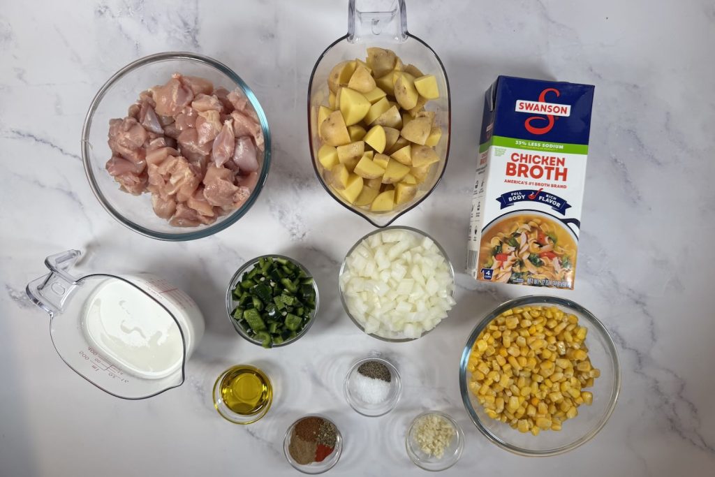 Ingredients for chicken poblano corn chowder including chicken, potatoes, corn, poblano peppers, onion, broth, cream, and spices.