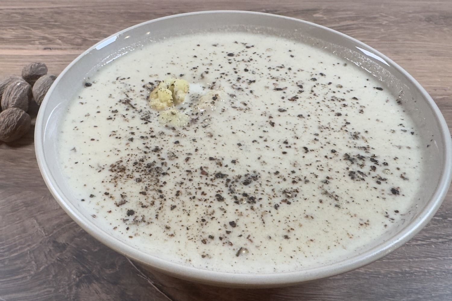 Bowl of creamy cauliflower soup topped with cracked black pepper.