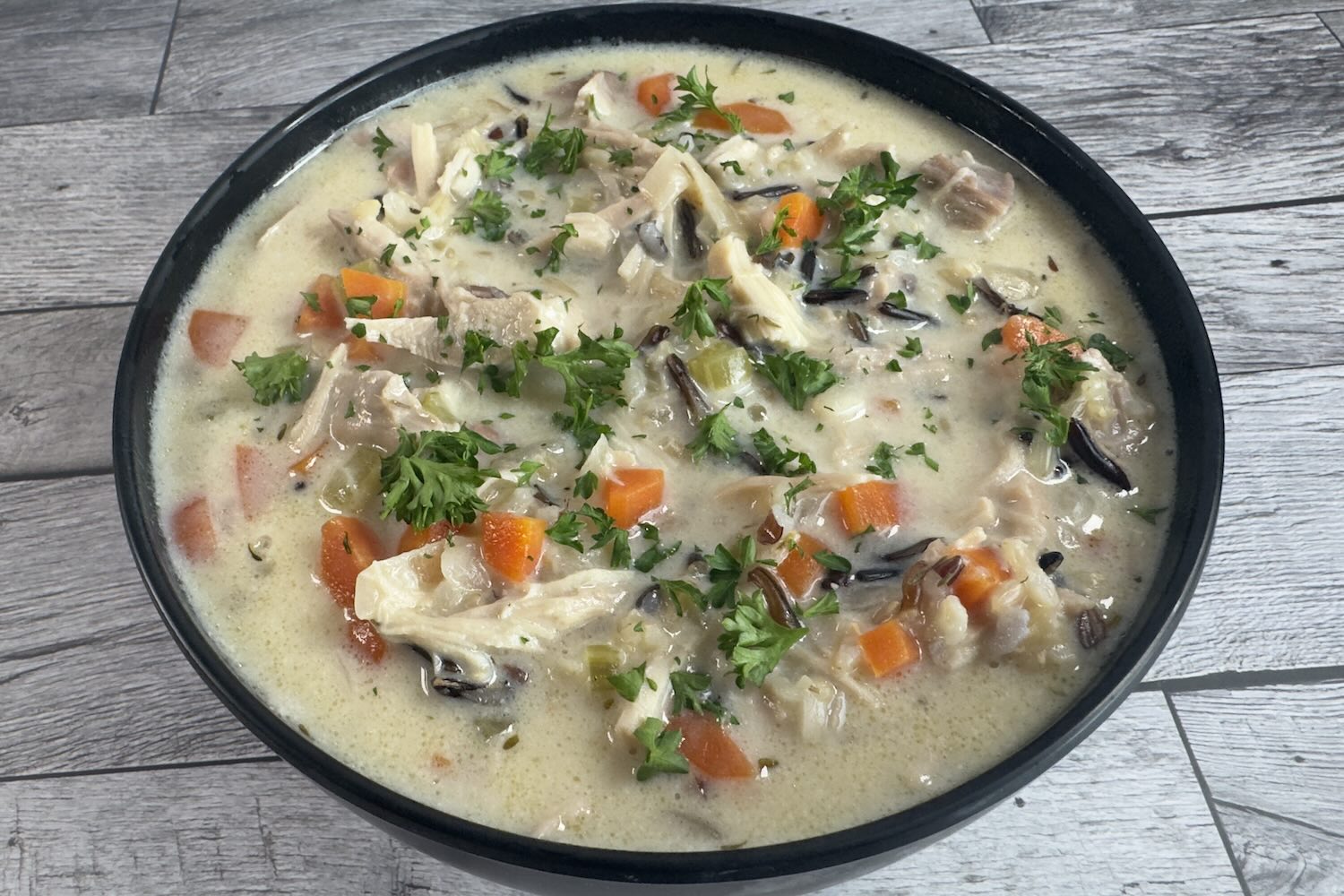 Bowl of creamy chicken and wild rice soup with shredded chicken, carrots, celery, and wild rice in a rich, creamy broth topped with fresh parsley.