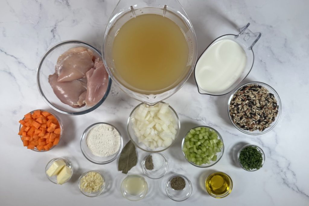 Ingredients for creamy chicken and wild rice soup including chicken, wild rice, chicken broth, milk, onion, celery, carrots, butter, flour, garlic, olive oil, lemon juice, parsley, and seasonings.