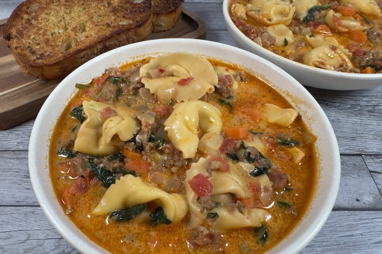 Bowl of creamy tortellini soup with sausage, spinach, carrots, and cheese-filled tortellini in a rich tomato cream broth, served with toasted bread.