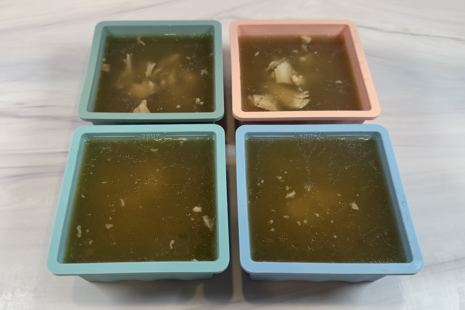 Portion containers filled with freezer-friendly chicken soup base made with broth and shredded chicken, ready for freezing.