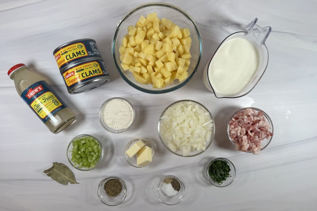 Ingredients for New England clam chowder including chopped clams, clam juice, potatoes, bacon, onion, celery, cream, butter, flour, and seasonings.