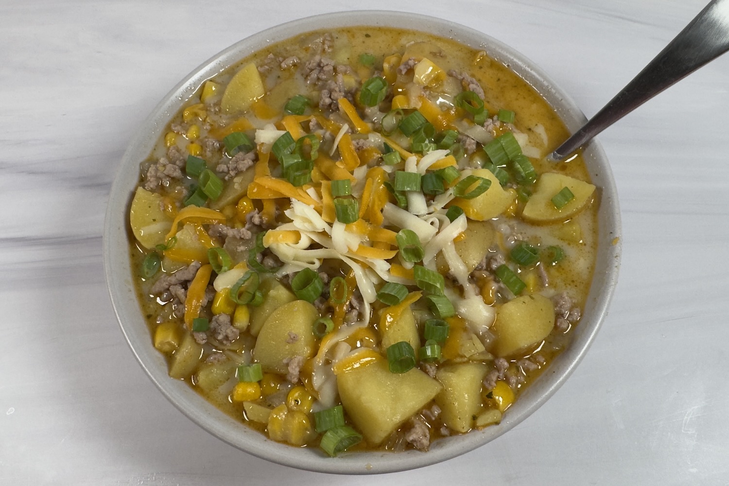 Bowl of Santa Fe pork and potato soup with ground pork, potatoes, corn, and green onions in a creamy broth, topped with shredded cheese.