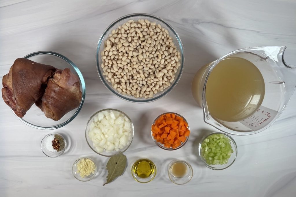 Ingredients for ham and bean soup including ham hocks, white beans, chicken broth, onion, carrots, celery, garlic, and seasonings.