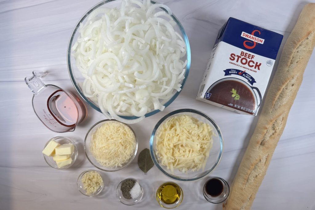 Ingredients for French onion soup including sliced onions, beef stock, Gruyère cheese, Parmesan cheese, baguette, sherry, garlic, butter, and seasonings.