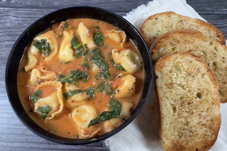 Bowl of creamy tomato tortellini soup with cheese tortellini and spinach in a rich tomato cream broth, served with toasted garlic bread.
