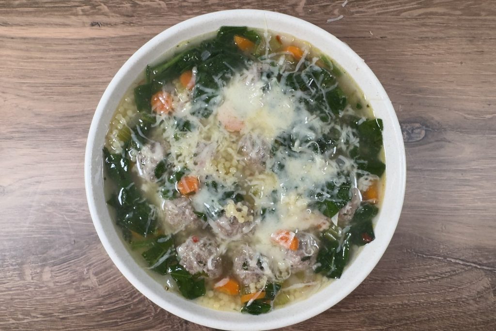 Bowl of Italian wedding soup with mini meatballs, spinach, carrots, tiny pasta, and grated Parmesan in a light savory broth.