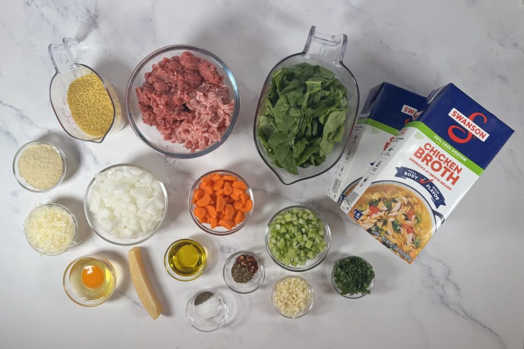 Ingredients for Italian wedding soup including ground meat, spinach, chicken broth, acini di pepe pasta, onion, carrots, celery, egg, Parmesan, breadcrumbs, garlic, parsley, olive oil, and seasonings.