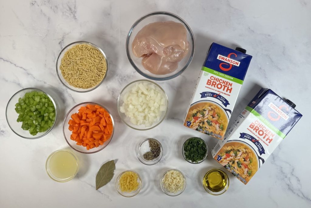 Ingredients for lemon chicken orzo soup including chicken breasts, orzo pasta, carrots, celery, onion, chicken broth, garlic, lemon juice, and fresh herbs.