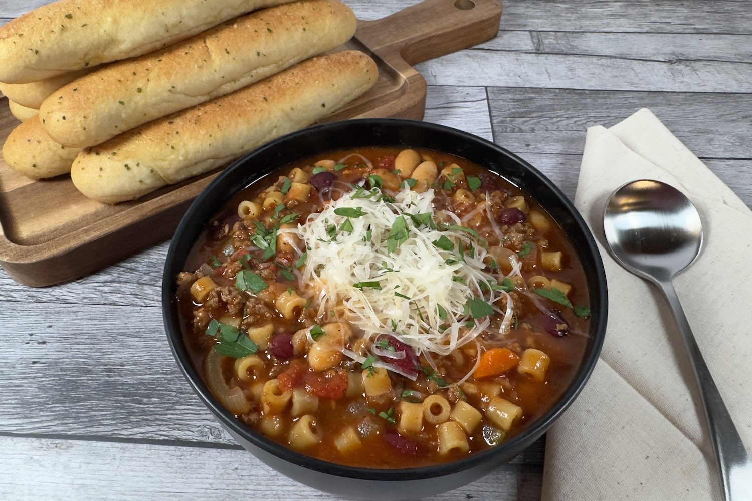 Bowl of pasta e fagioli topped with Parmesan cheese and parsley, with ground beef, beans, pasta, vegetables, and tomatoes in a rich broth.