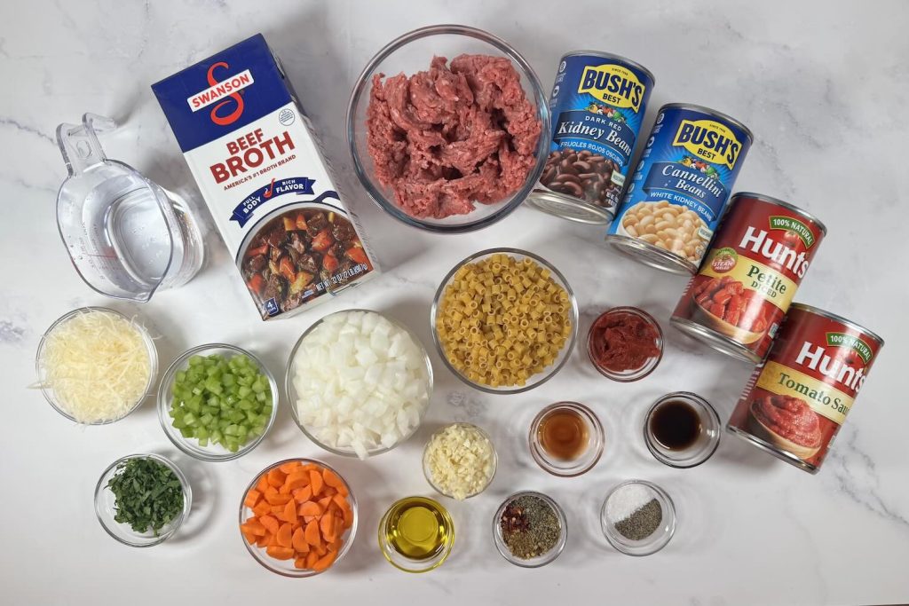 Ingredients for pasta e fagioli including ground beef, ditalini pasta, kidney beans, cannellini beans, diced tomatoes, tomato sauce, beef broth, onion, carrots, celery, garlic, Parmesan, and seasonings.