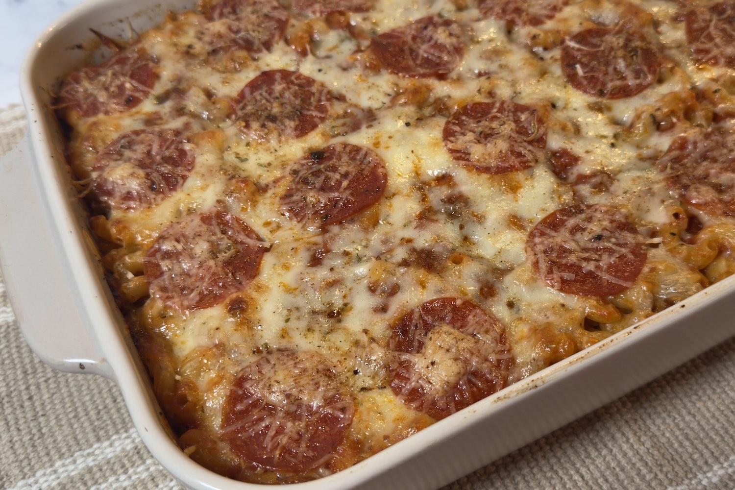 Baked easy pizza casserole in a white baking dish topped with melted cheese, pepperoni slices, and a sprinkle of Parmesan.