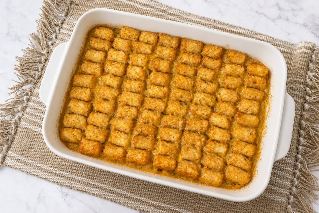 Baked tater tot casserole in a white baking dish with golden crispy tater tots over a creamy ground beef, green bean, and cheddar cheese filling.