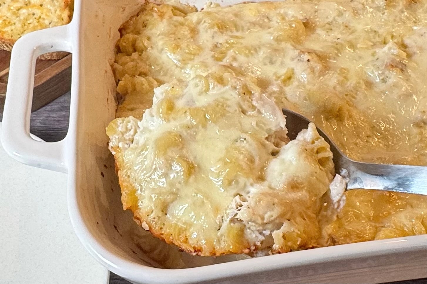Chicken Alfredo Bake served from a white casserole dish, with tender rotini pasta, chicken, and a creamy Alfredo sauce topped with melted mozzarella cheese.