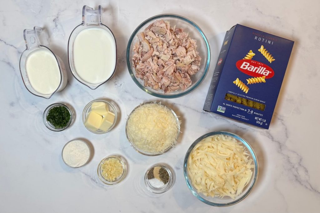 Ingredients for Chicken Alfredo Bake including rotini pasta, cooked chicken, milk, heavy cream, mozzarella cheese, Parmesan cheese, butter, garlic, parsley, flour, salt, and black pepper.