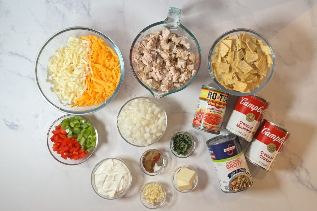 Ingredients for king ranch chicken casserole including cooked chicken, corn tortillas, cheddar cheese, Monterey Jack cheese, onion, bell peppers, Rotel, cream of mushroom soup, cream of chicken soup, chicken broth, sour cream, garlic, butter, cilantro, and seasonings.
