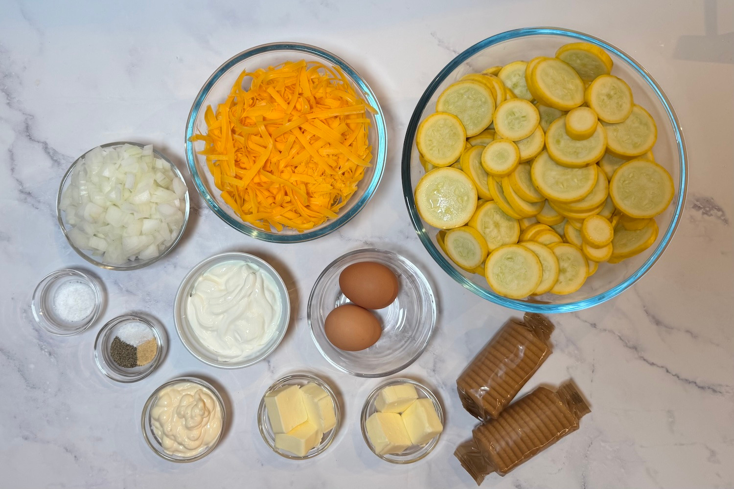 Ingredients for southern summer squash casserole including yellow squash, onion, cheddar cheese, sour cream, mayonnaise, eggs, butter, crackers, salt, pepper, and seasonings.